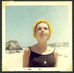 a woman in a black top and yellow hair is standing on the beach with her eyes closed