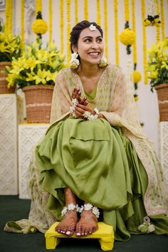 a woman sitting on top of a yellow bench wearing a green dress and flower garlands