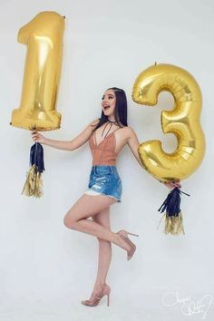 a woman holding two large gold balloons in the shape of numbers, and wearing high heels