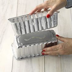 two hands holding aluminum pans on top of a white wooden table with wood flooring