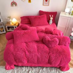 a bed with pink comforters and pillows in a room next to a white rug