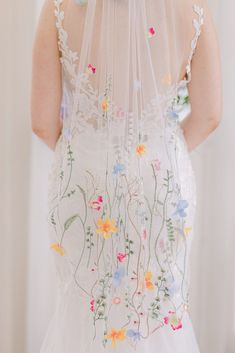 the back of a bride's dress with flowers on it and a veil over her head