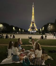 group of people sitting on blanket in front of the eiffel tower at night