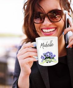 a woman in sunglasses is holding a coffee mug and talking on her cell phone while smiling at the camera