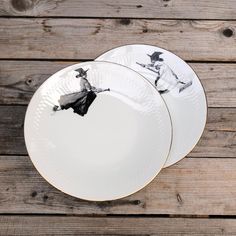 two white plates with black designs on them are sitting on a wooden table, next to each other