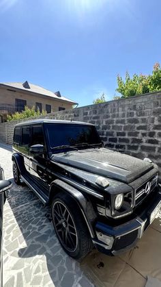 a black mercedes g - class parked in front of a brick wall and stone walkway