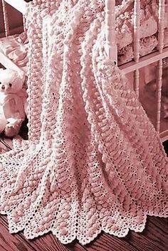 there is a crocheted blanket on the floor next to a teddy bear in a crib