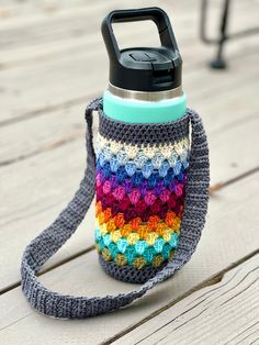 a multicolored crocheted water bottle cover sitting on top of a wooden table