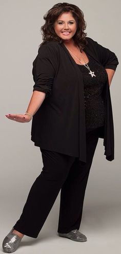 a woman in black is posing with her hands on her hip and smiling at the camera