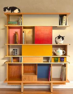 two cats sitting on top of a bookshelf next to a coffee cup and vase