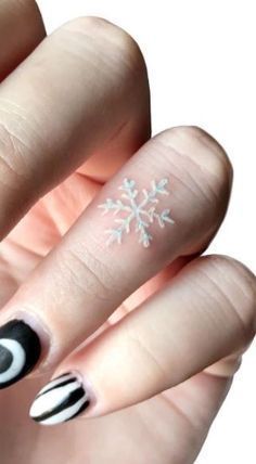 a woman's hand with black and white nail polish on it, decorated with snowflakes