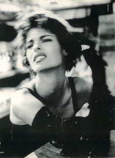 a black and white photo of a woman with her hair blowing in the wind while sitting at a table