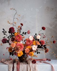 a vase filled with lots of flowers sitting on top of a white cloth covered table