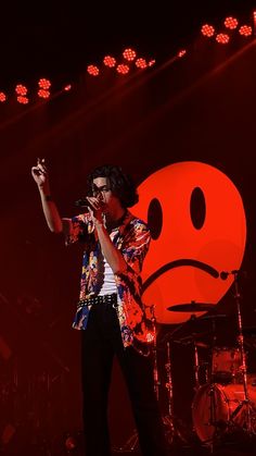 a man standing on top of a stage next to a red smiley face wallpaper