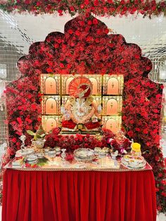 a table topped with lots of food next to a red flower covered wall behind it