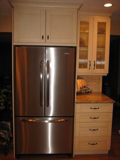 a metallic refrigerator freezer sitting inside of a kitchen next to white cupboards and drawers