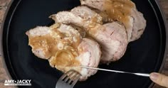 a person is holding a fork over some meat on a plate with gravy