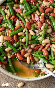 beans, green beans and onions in a white bowl with a spoon on the side