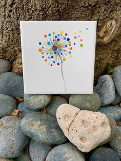 a white tile with a colorful dandelion painted on it next to some rocks