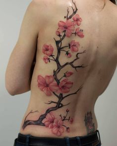 a woman's back with pink flowers on her body and behind it is a tree branch