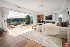 a large living room with wood floors and white furniture, overlooking the water from an open floor - to - ceiling window