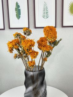 a vase filled with yellow flowers sitting on top of a white table next to framed pictures