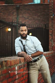 a man leaning against a brick wall with his hands on his hips wearing a tie