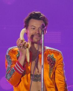 a man holding a banana up to his face while standing in front of a microphone