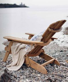 a wooden lawn chair sitting on top of a pebble covered beach next to the ocean