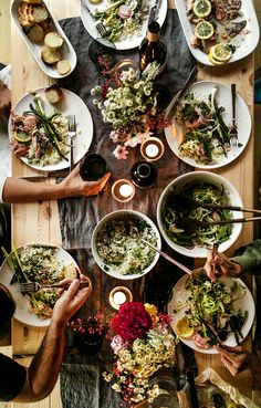 several people are eating dinner at a table with plates and bowls on it, while the rest of the table is covered in food