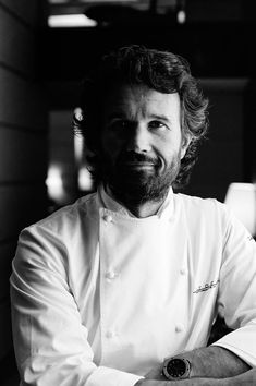 a man with long hair and beard wearing a white chef's coat is posing for the camera