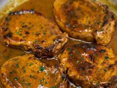 three pieces of meat covered in gravy on top of a pan filled with sauce