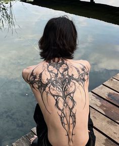 a woman sitting on a dock with her back turned to the camera, looking at water