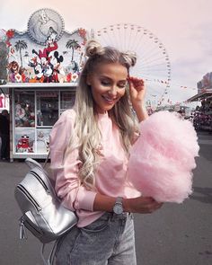 a woman holding a pink heart shaped lollipop in front of a carnival ride