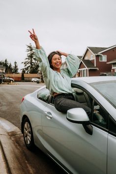 a woman is sitting on top of a car and waving to the side with her hands in the air