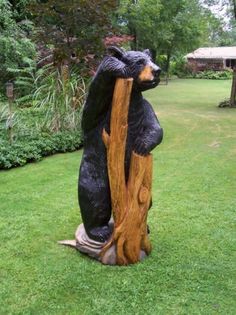 a bear statue sitting on top of a tree stump in the grass next to a house