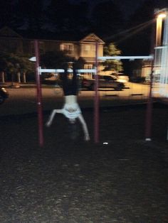 a person is doing tricks on a pole in the street at night with cars parked behind them