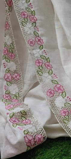 the white fabric with pink flowers is on top of green grass and has lace trim around it