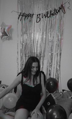 a woman sitting on top of a bed in front of balloons and streamers that say happy birthday