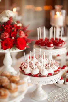 there are many desserts on the table with red roses in the vase behind them