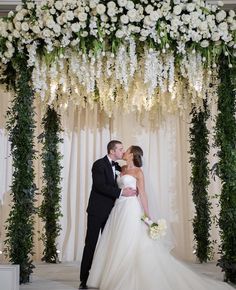 a bride and groom kissing under a floral arch