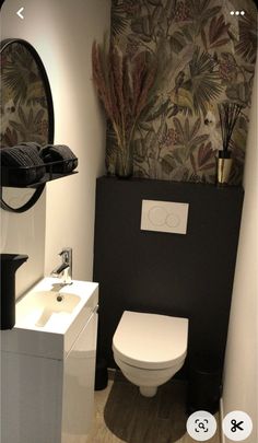 a white toilet sitting next to a sink in a bathroom under a wallpapered mirror