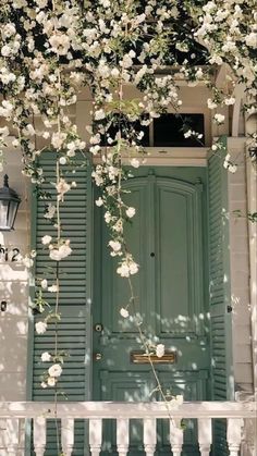 a green door with white flowers growing over it and a light fixture on the side