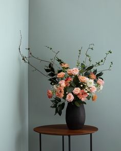 a black vase filled with pink and white flowers on top of a small round table