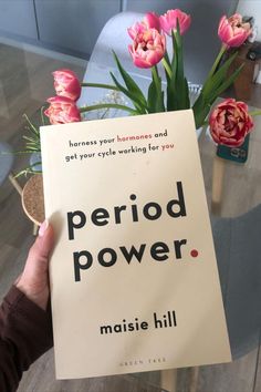 a person holding up a book with flowers in the background and an advertisement for period power written on it