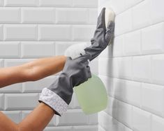 a person wearing gloves and cleaning mitts with a sponge on a white tiled wall