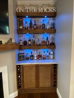 an entertainment center with liquor bottles on the shelves and lights in the bottom shelf that says on the rocks