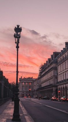 a street light sitting on the side of a road next to tall buildings at sunset