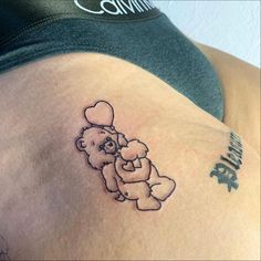 a tattoo on the back of a woman's shoulder with a teddy bear holding a heart