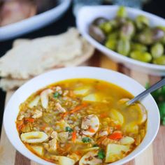 there is a bowl of soup with vegetables and bread on the table next to it